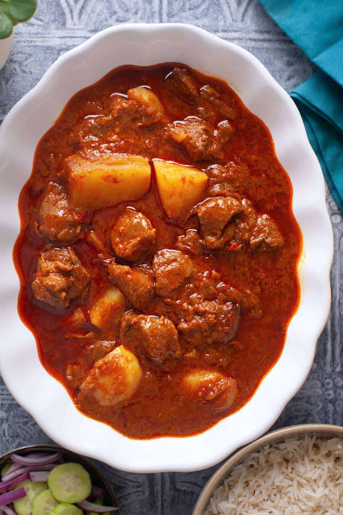 Top view of aloo gosht served with cumin rice and salad.