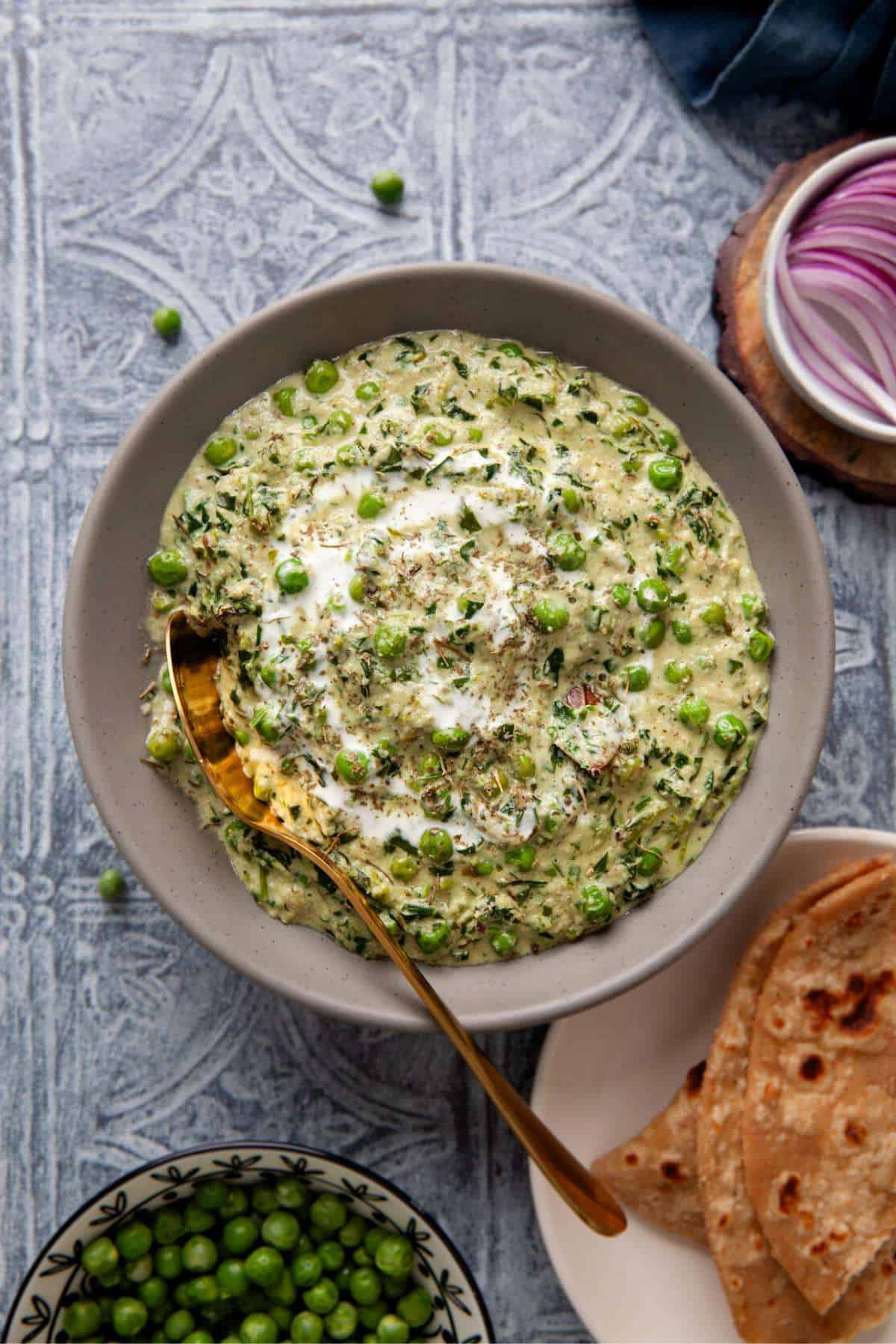 Methi Matar Malai in a grey bowl served with sliced onion and flatbreads.