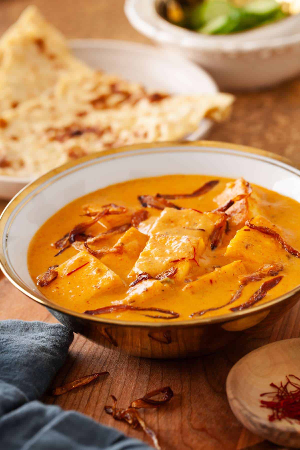 Shahi Paneer Korma in a white and gold bowl with naan in background.