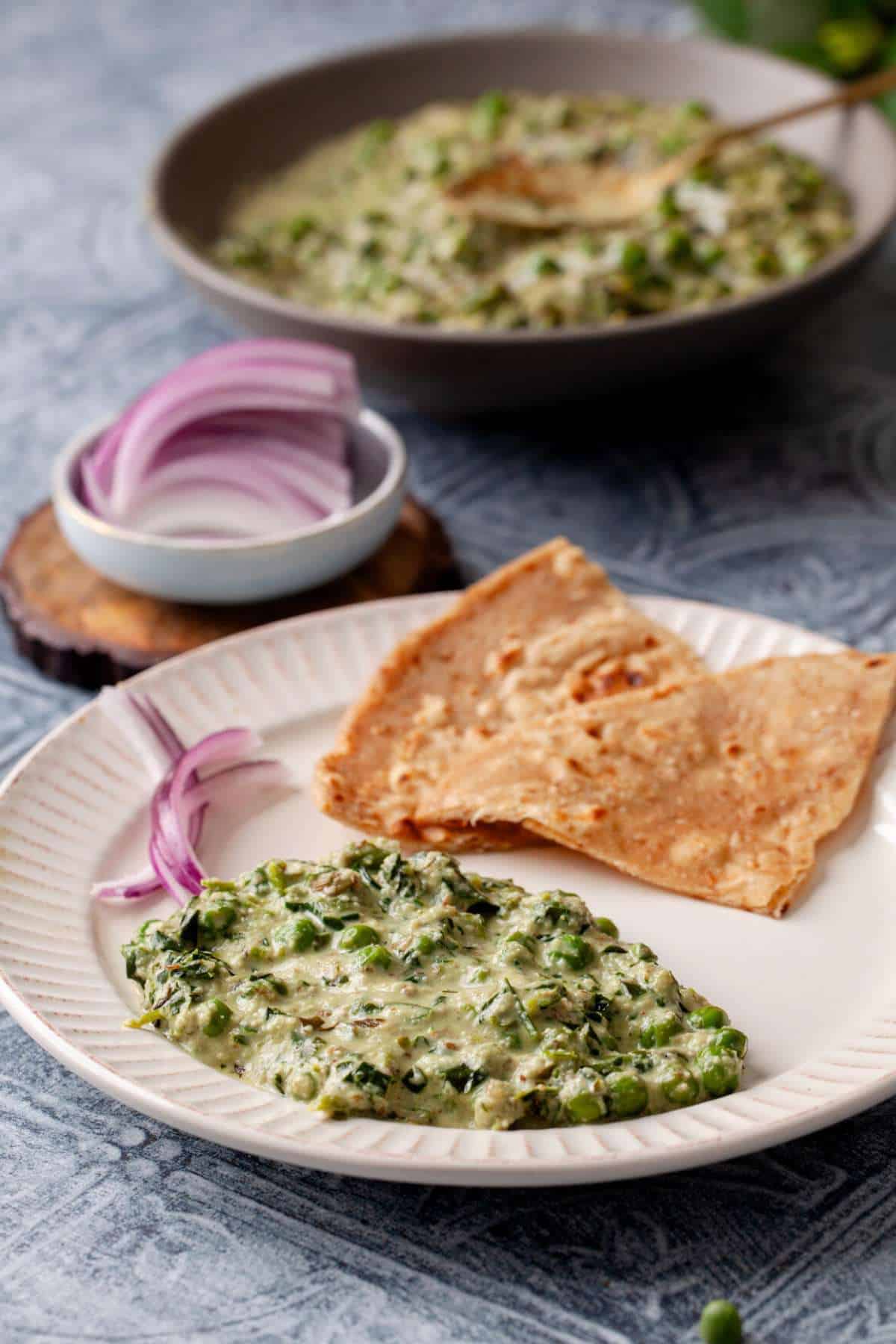 Methi Matar Malai curry served with a flatbread on a white plate. 