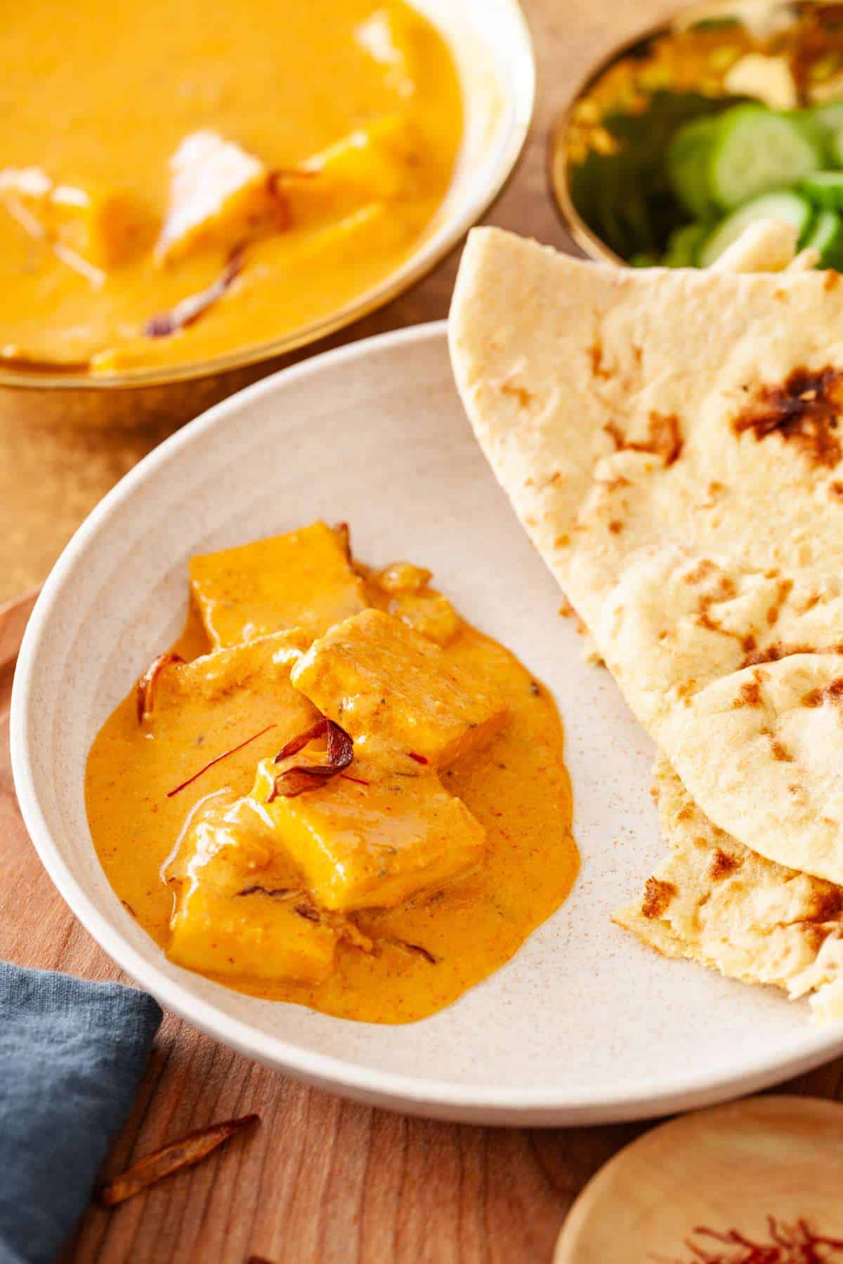 Paneer korma served with naan on a beige colored plate.