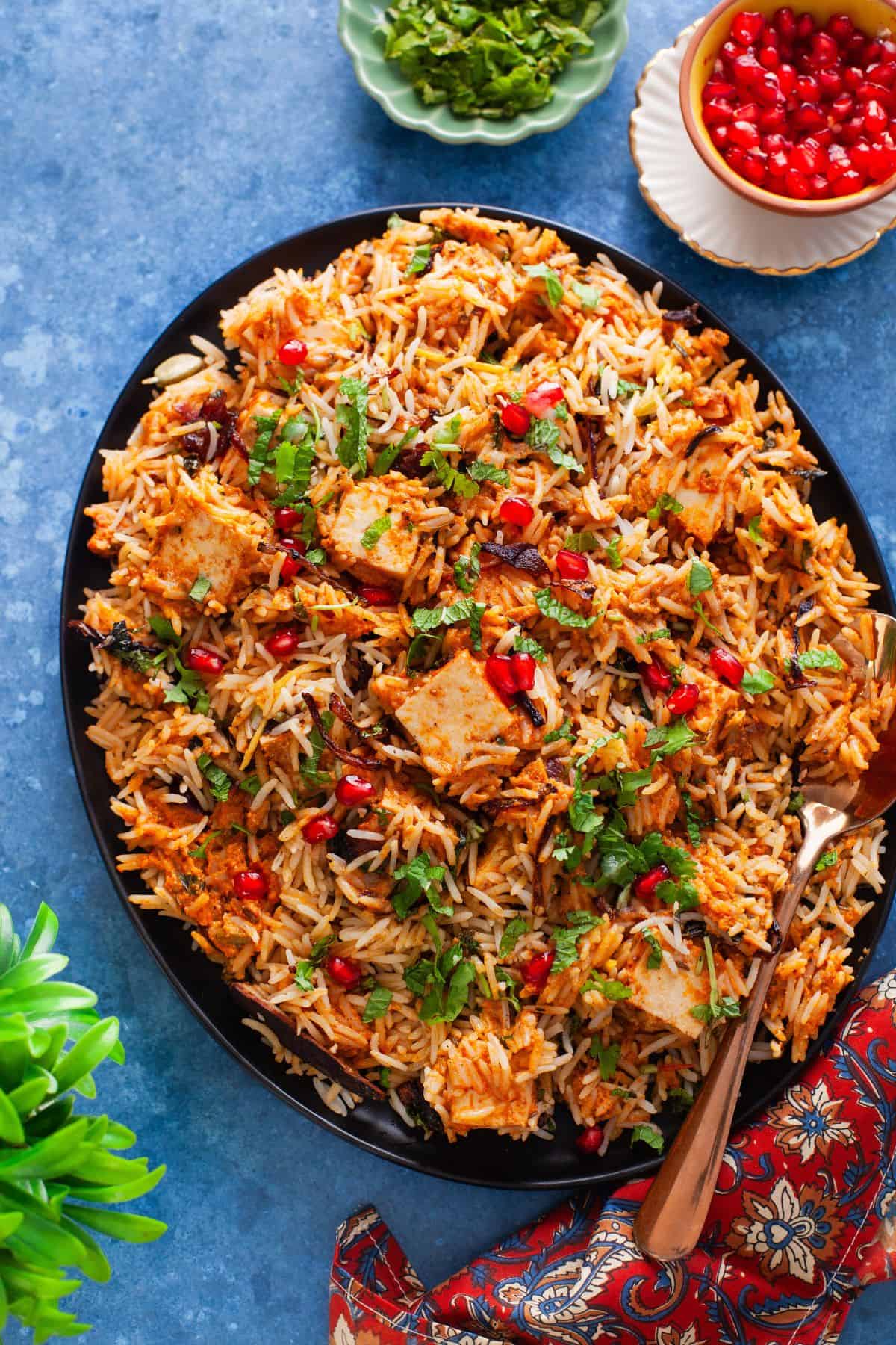 Makhani Paneer biryani plated in a black plate and place on a blue background.