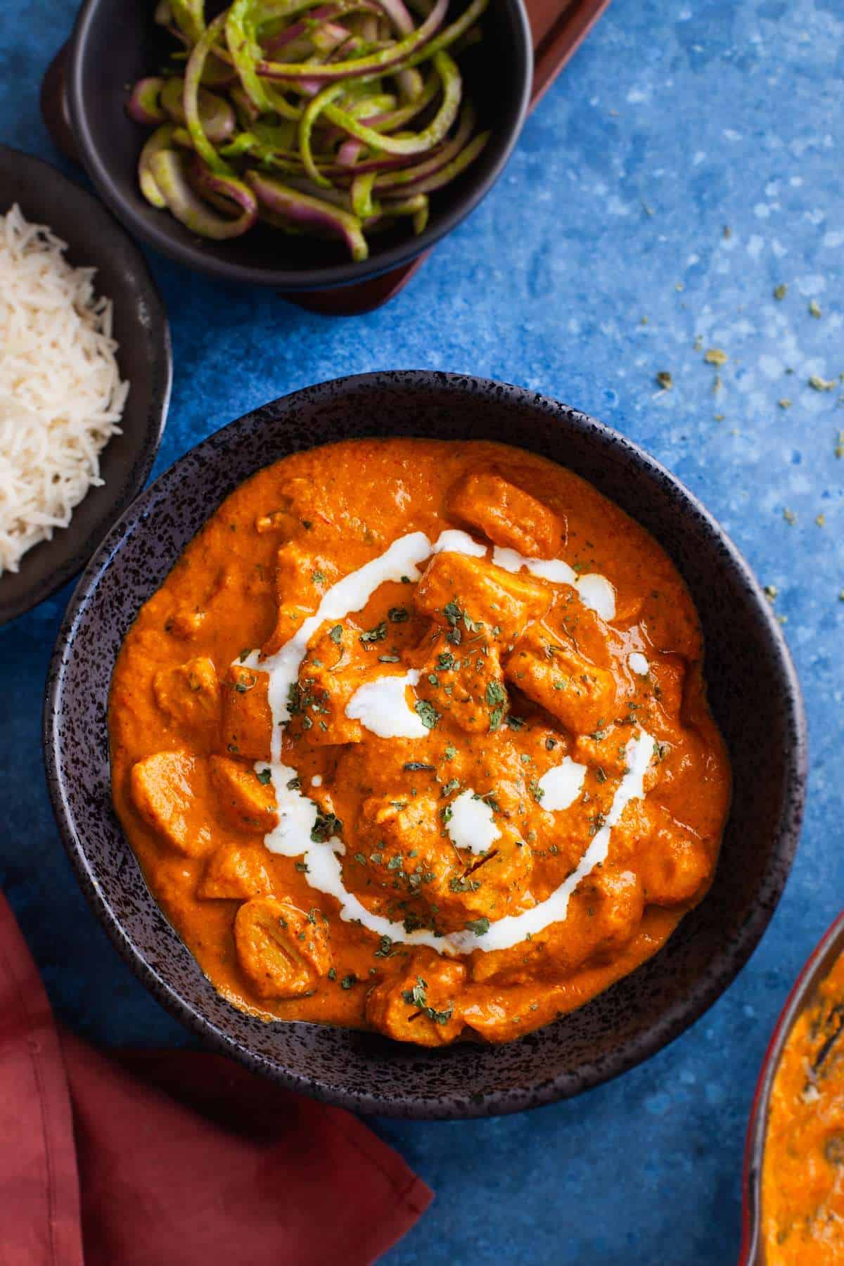 Makhani Soya Chaap in a black bowl with rice and onion salad. 