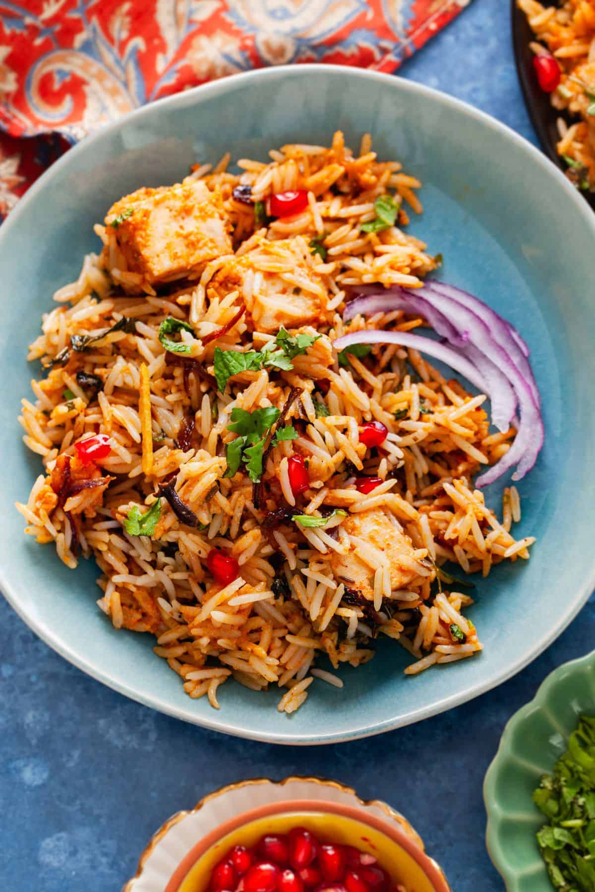 Paneer biryani plated in a blue plate with onion slices.