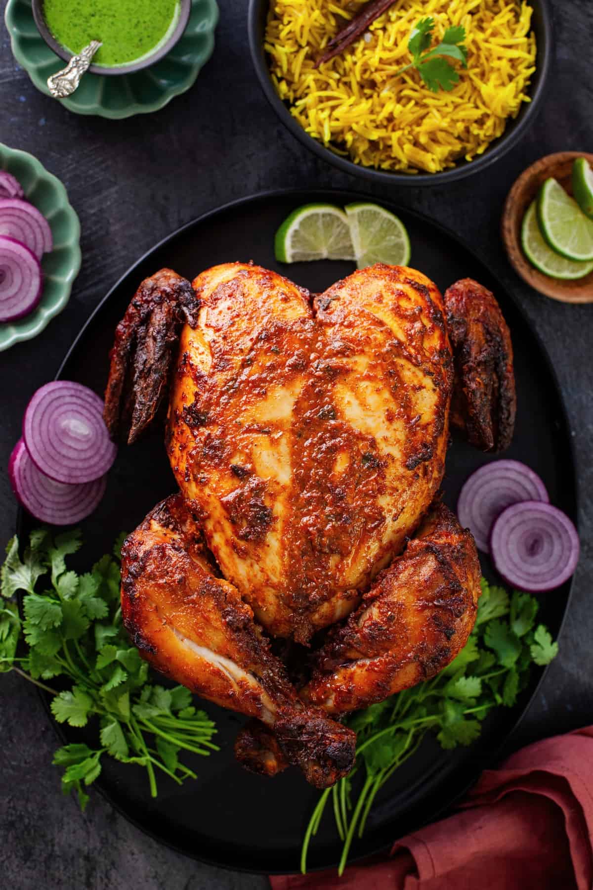 Tandoori chicken served with yellow rice, green chutney, sliced onion and lemon wedges.