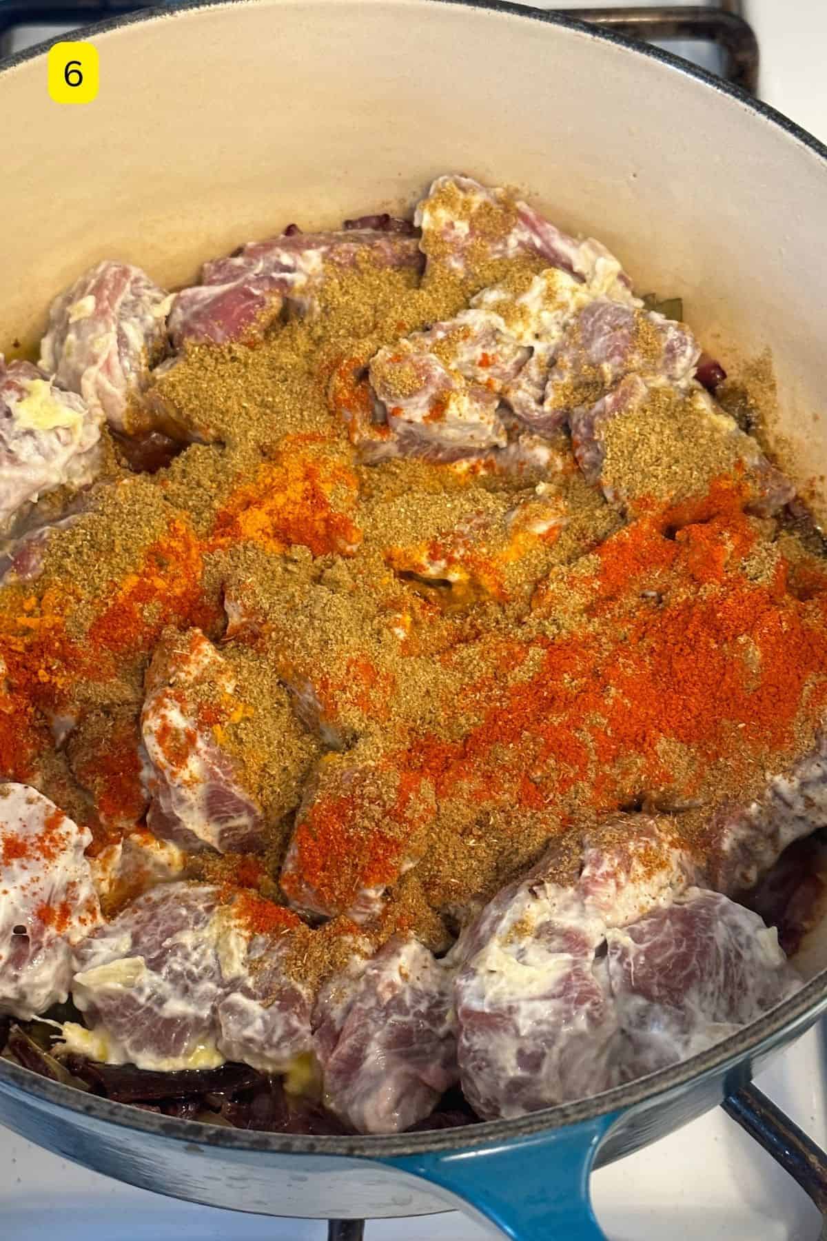 Mainated lamb with ground spices added to the cooking pot.