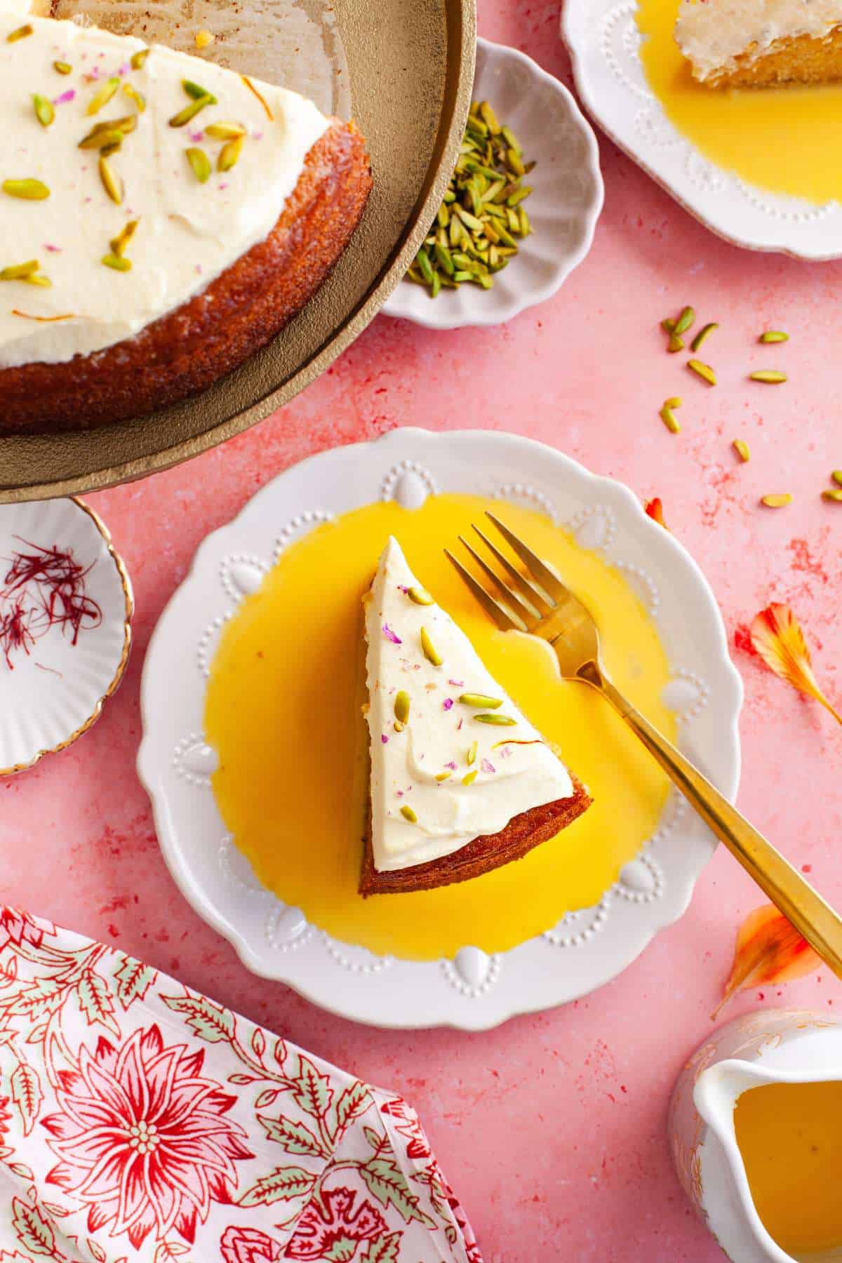 Mango Rasmalai cake slice on a white lace plate with mango milk ras.
