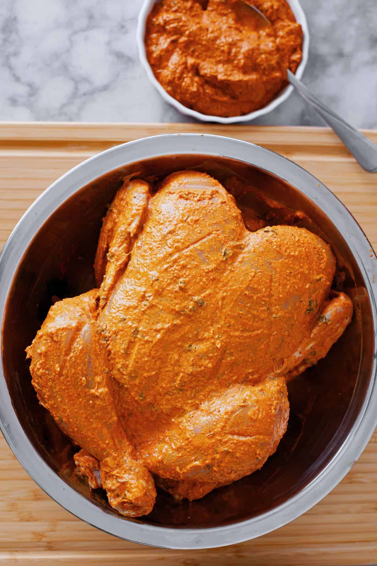 Raw whole chicen covered in a tandoori marinade.