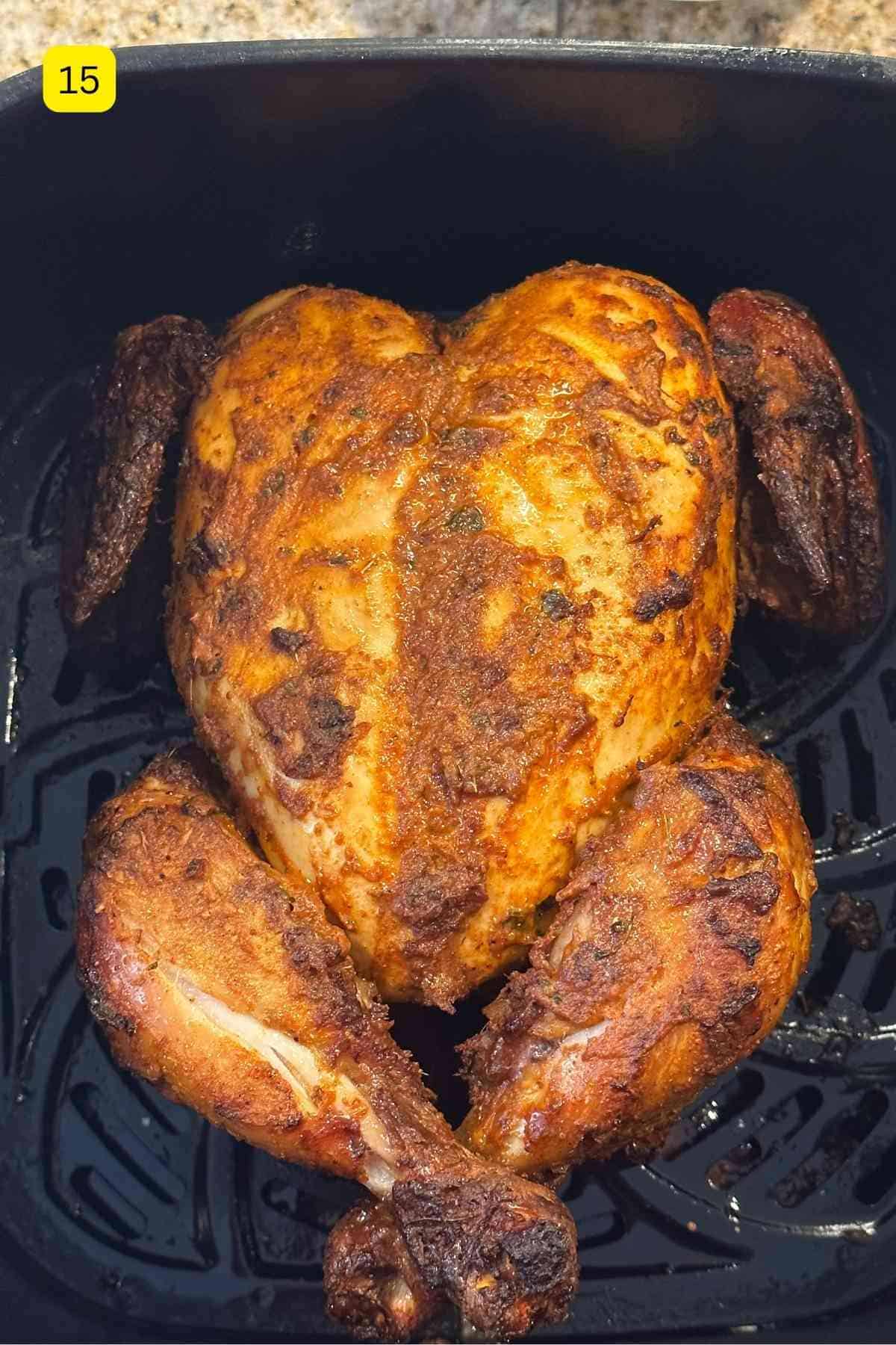 Air fyer whole tandoori chicken in a black basket.