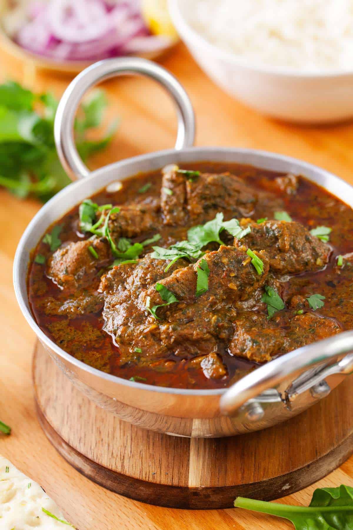 Side view of palak lamb with rice and sliced onion in background.