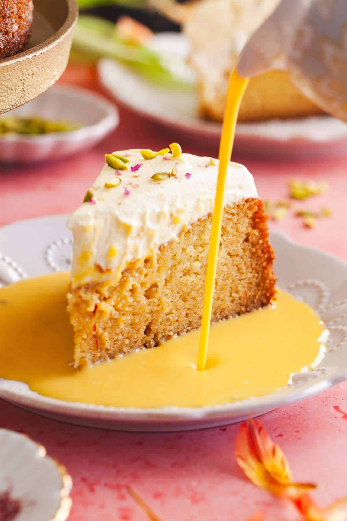 Mango Rasmalai cake slice served on a white plate with mango milk pour.