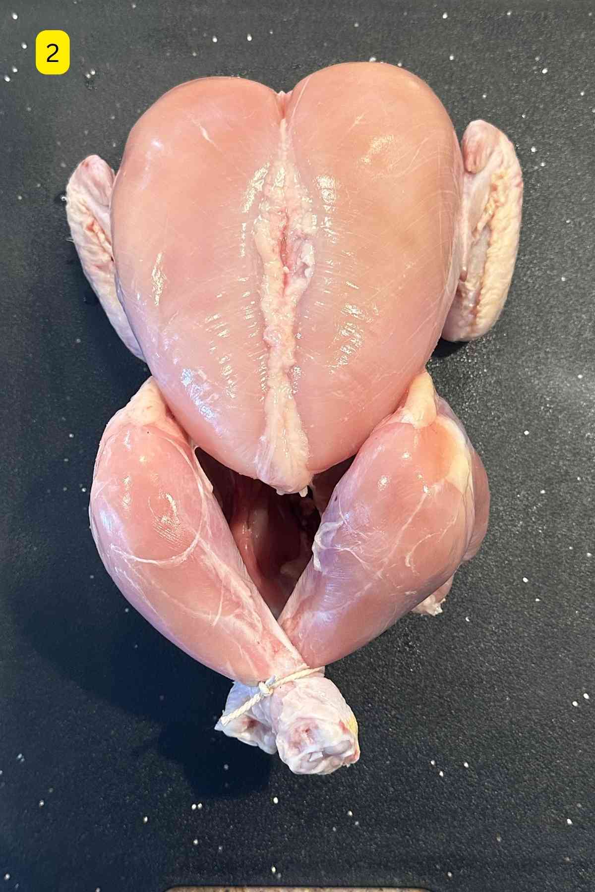 Skinned whole chicken placed on a ablack cutting board.