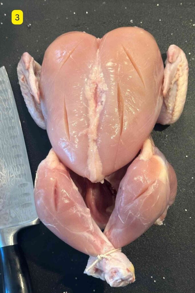 Whole chicken with deep cuts and slashes.