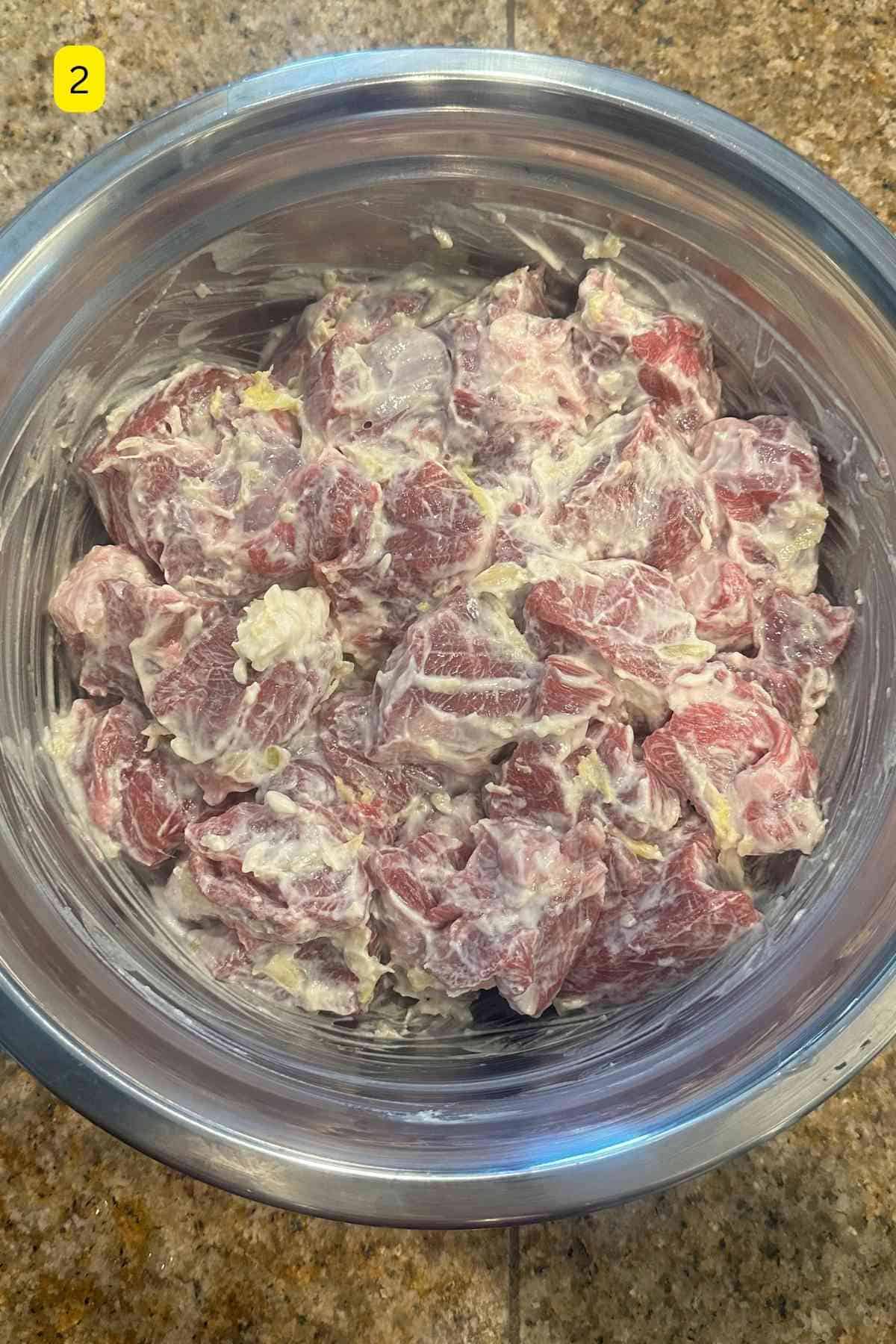 Marinated lamb meat in a large steel mixing bowl.