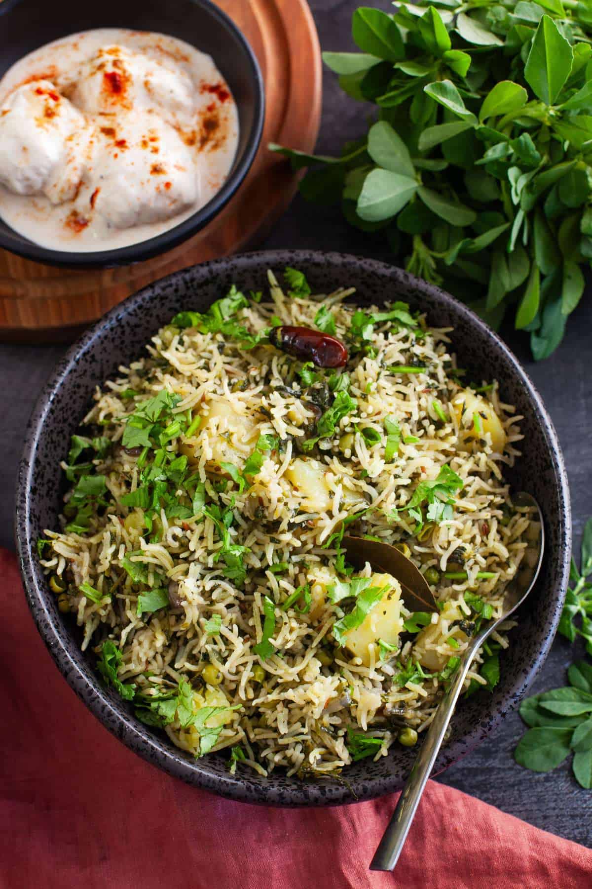 Methi pulao in a black bowl served with yogurt.