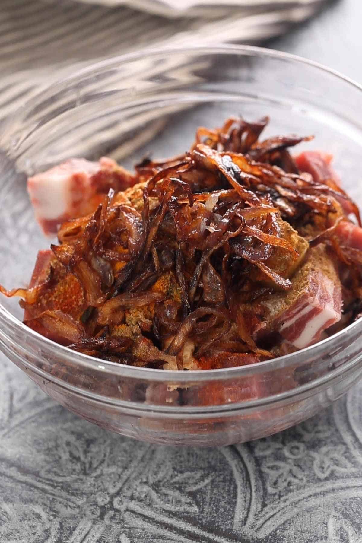Large glass bowl with mutton pieces and the marinade ingredients.
