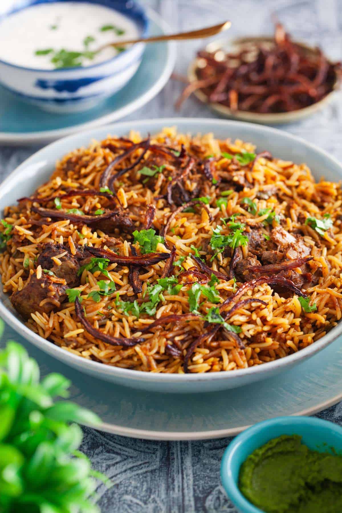 Side view of mutton biryai with yogurt raita in the background.