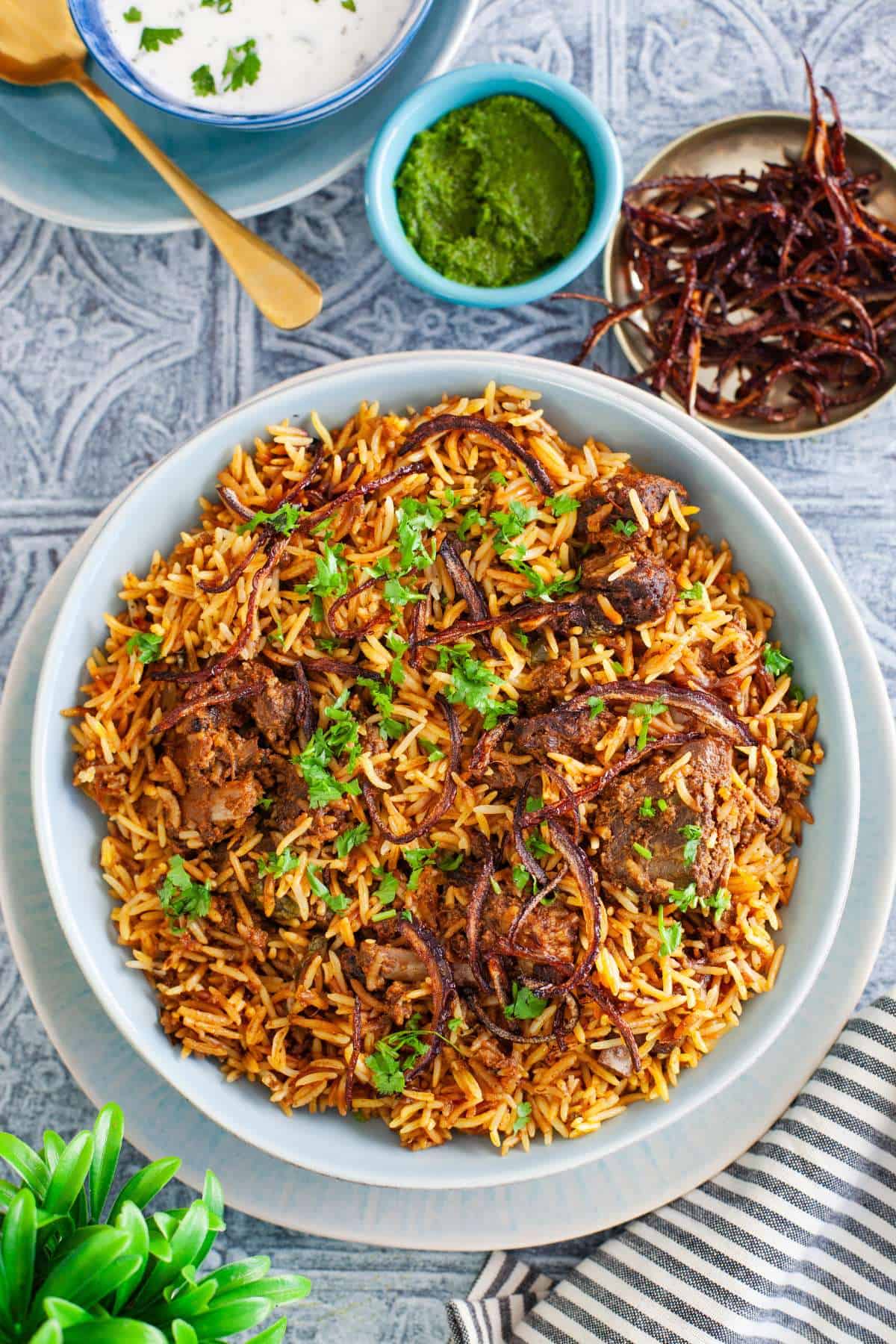 Mutton Biryani served in a large blue dish and topped with fried onions.