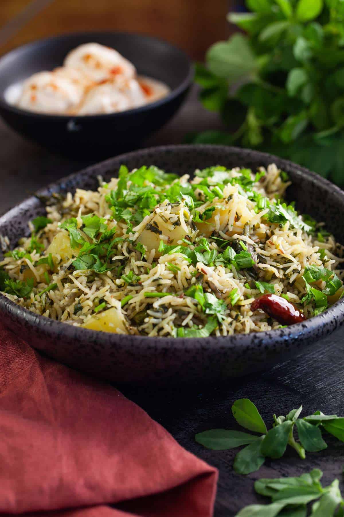 Side view of fenugreek pulao in a black bowl. 