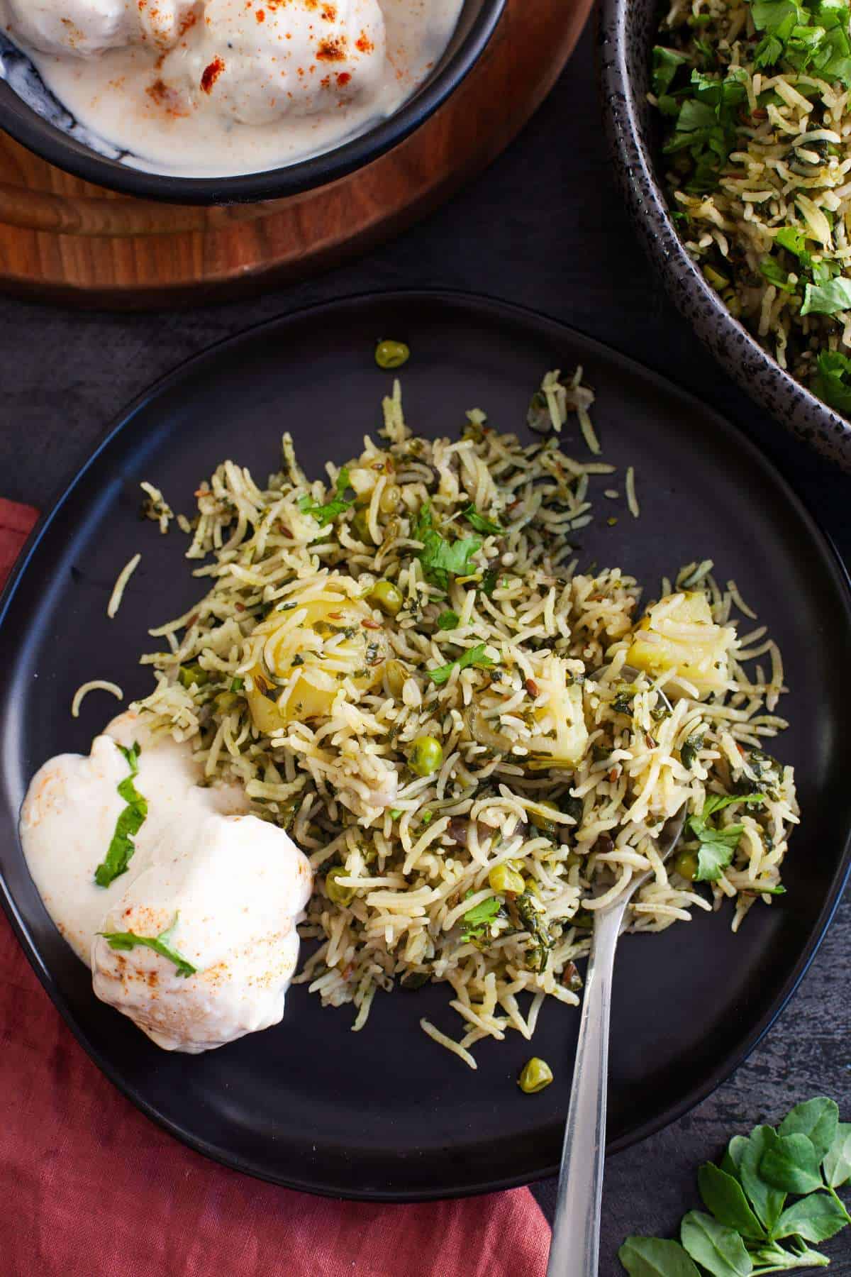 Methi pulao served with yogurt in a black plate. 
