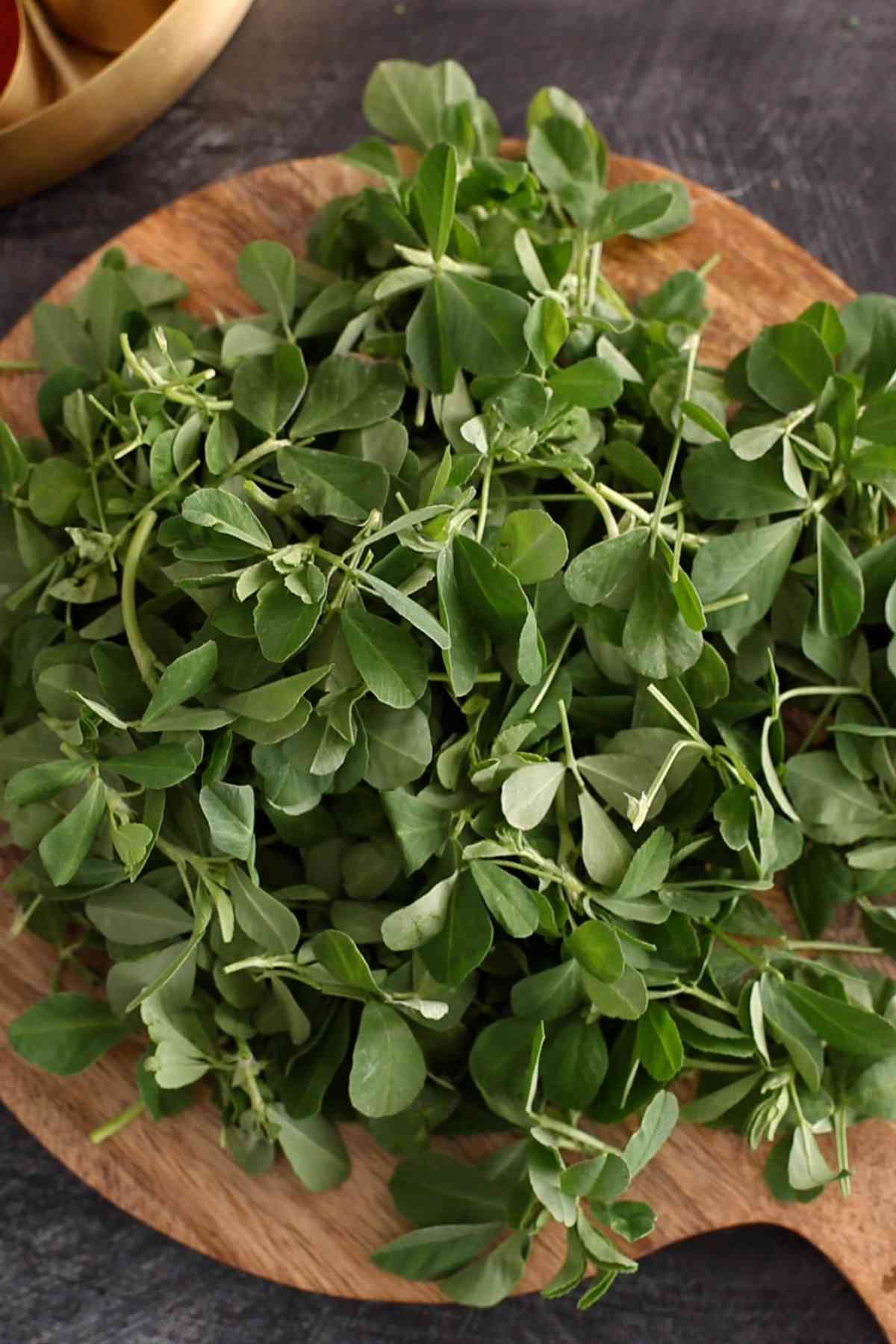 Fresh methi leaves on a wooden board.