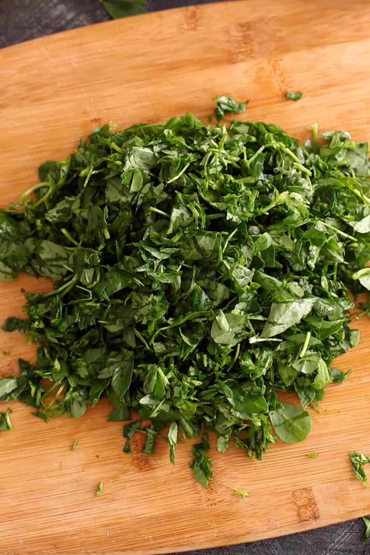 Chopped methi leaves on a bambo cutting board.
