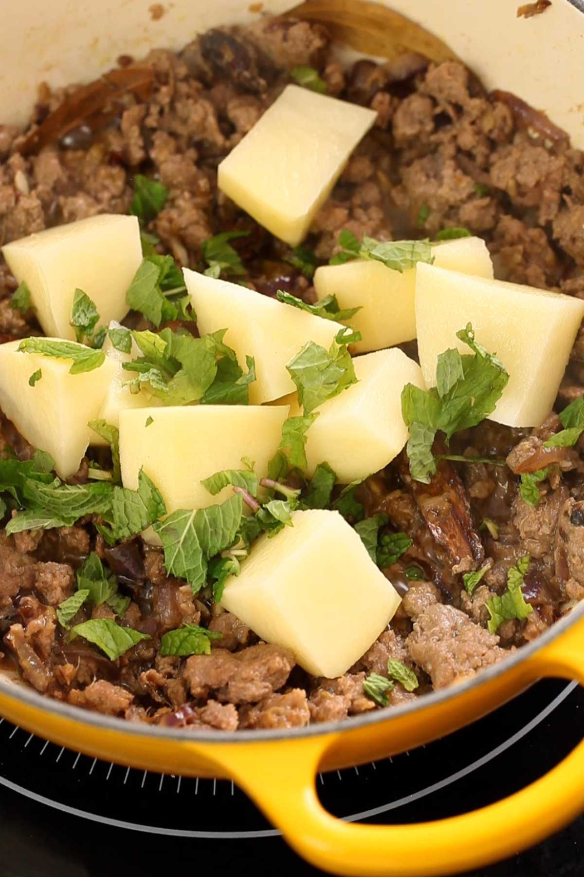Adding potatoes and fresh mint to the keema. 