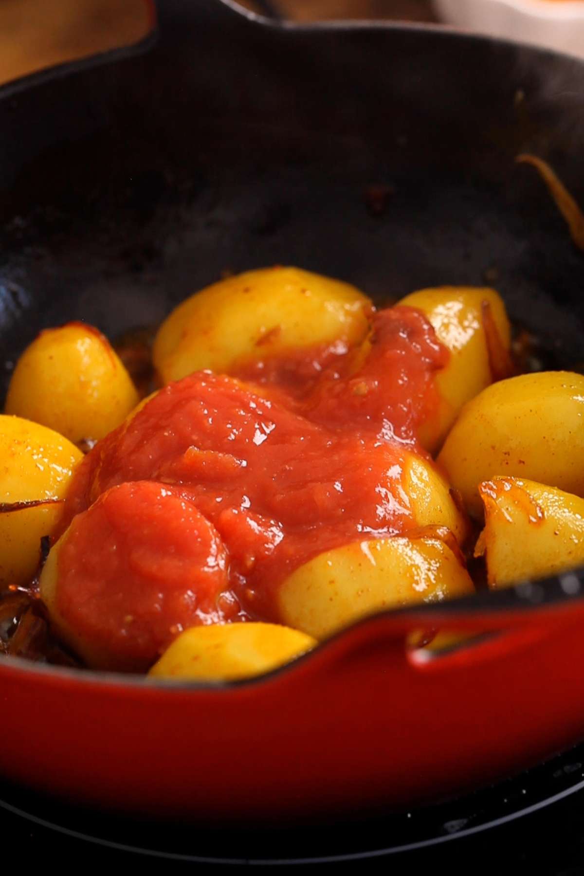 Adding tomato puree to the potatoes. 
