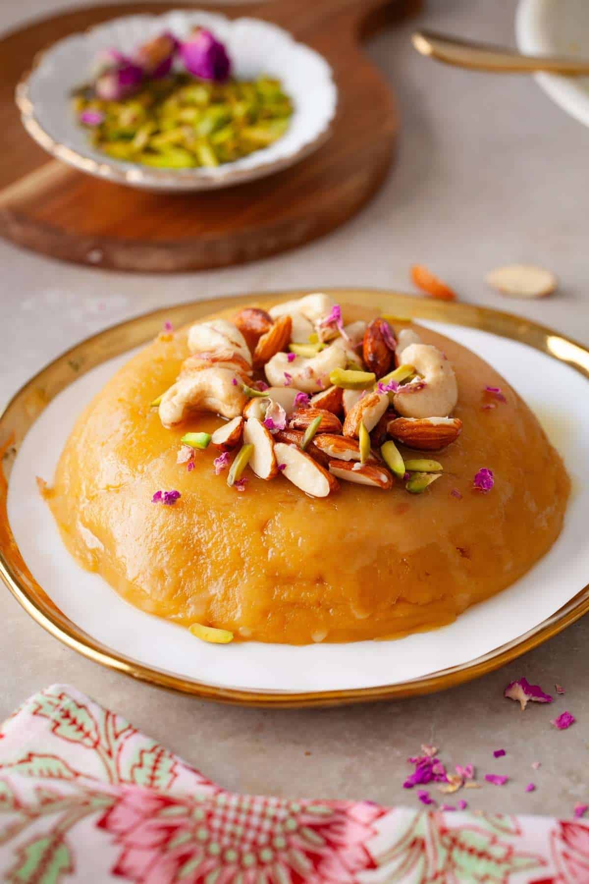 Besan halwa on a white, gold rimmed plate decorated with nuts. 