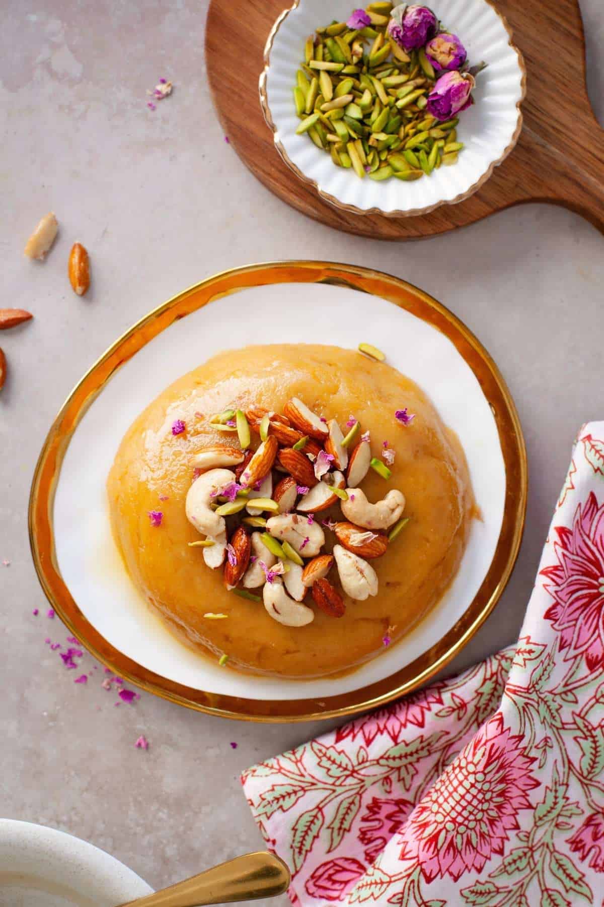 Top view of gram flour halwa with silvered pistachios and rose petals.