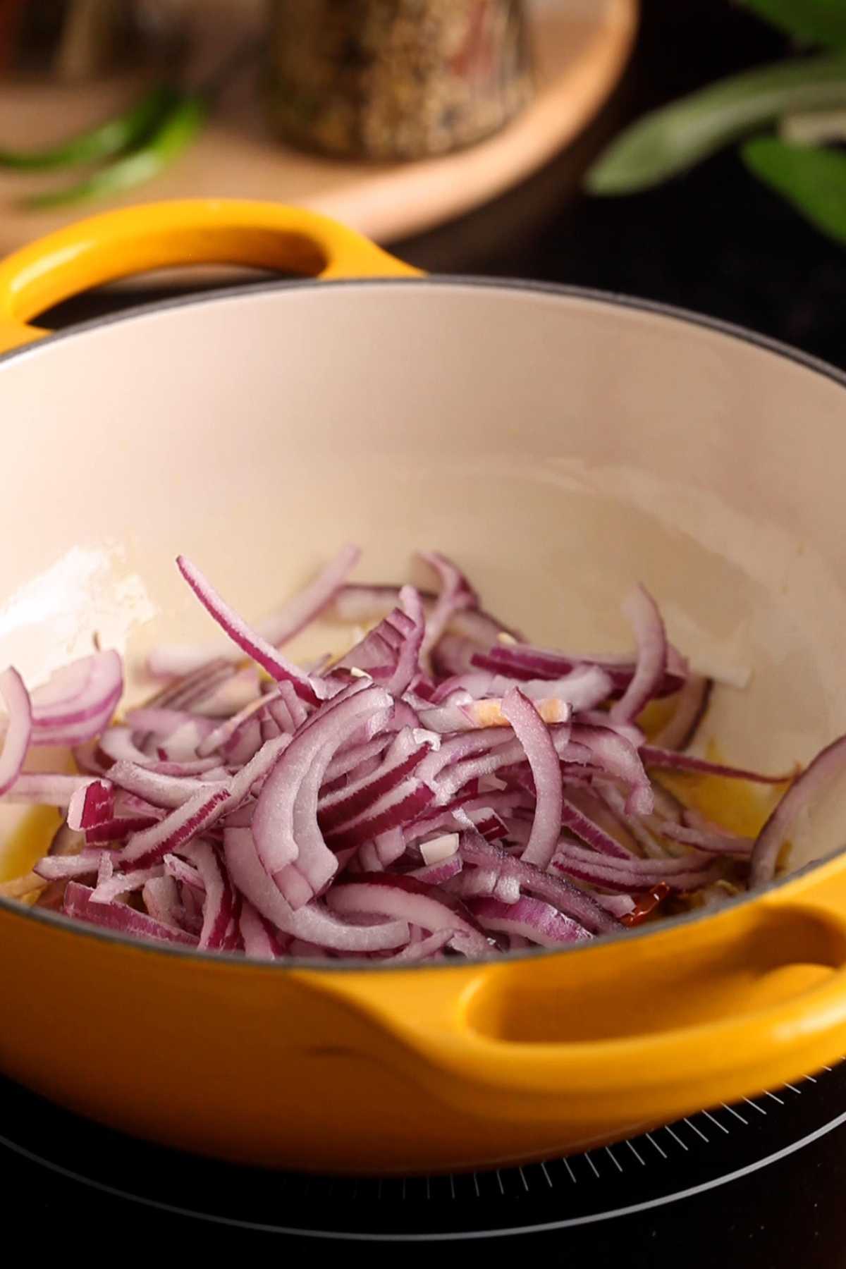 Adding sliced red onions to hot oil.