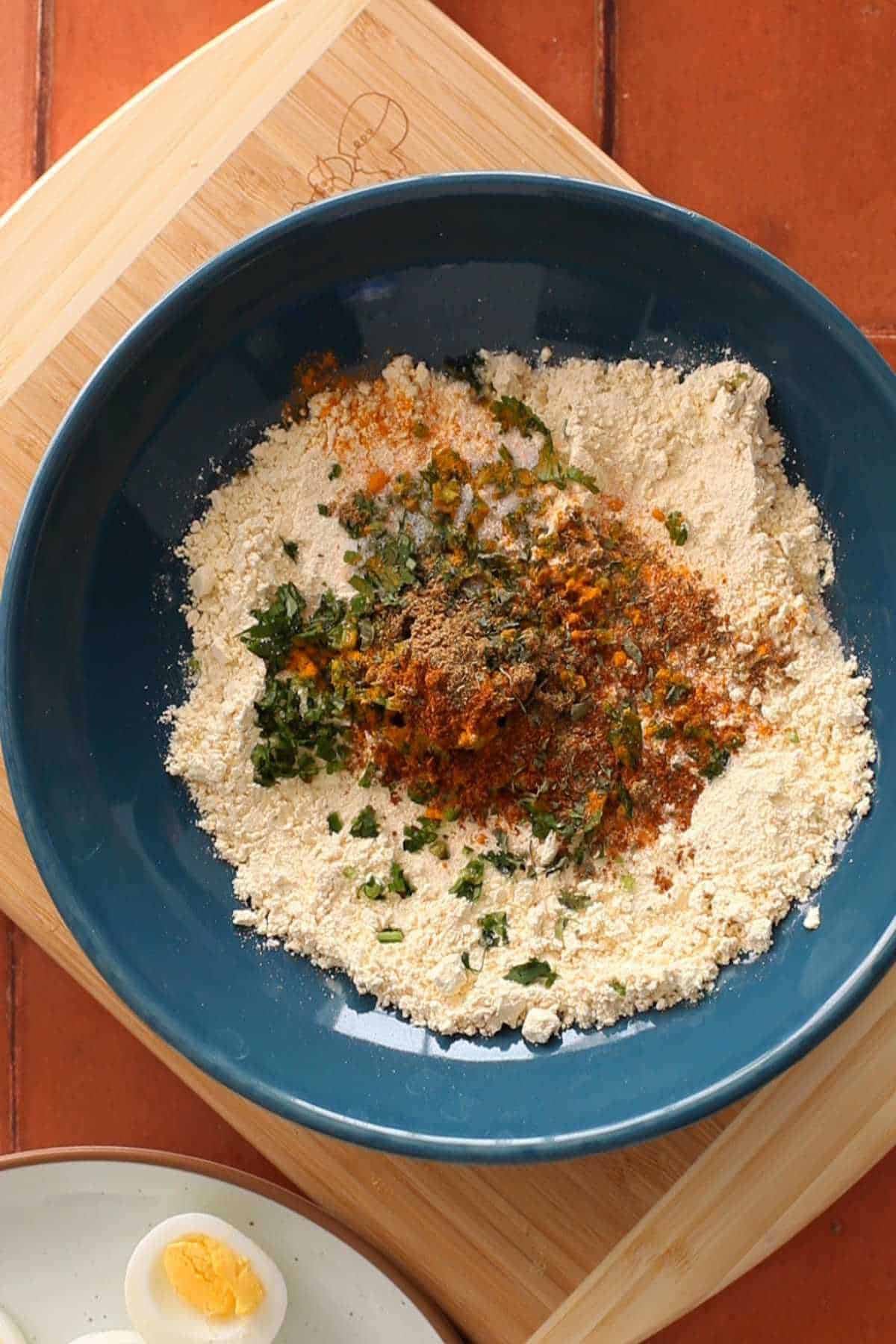 Gram flour in a blue bowl with all the herbs and spices.