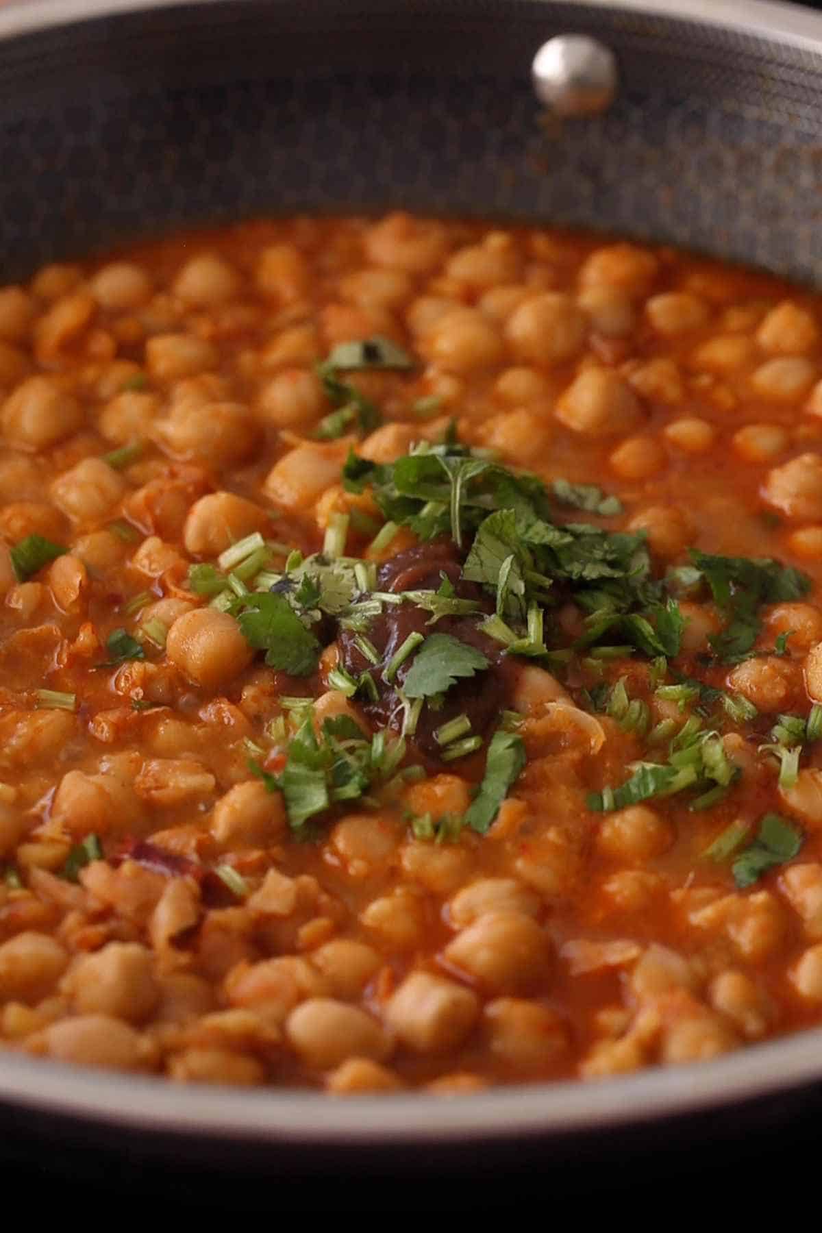 Adding chopped green herbs and tamarind to finish chana masala.