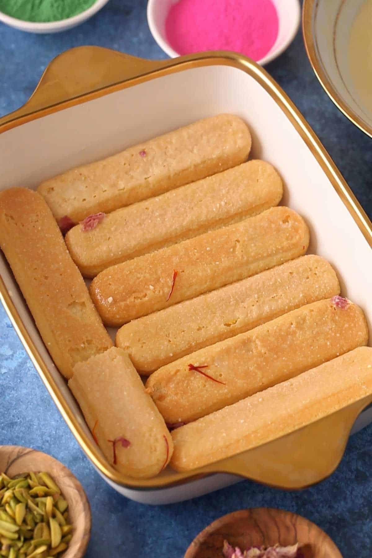 Placing first layer of lady finger cookies in a white and gold dish.