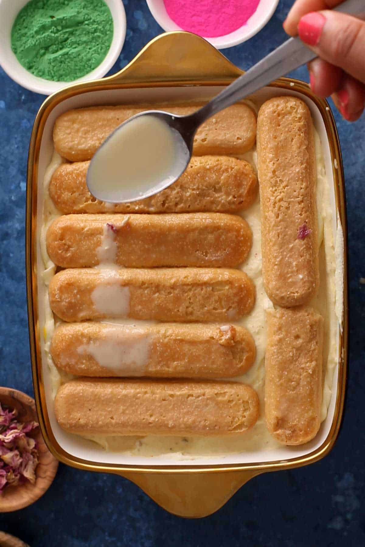Adding second layer of lady finger cookies and soaking in extra thandai.