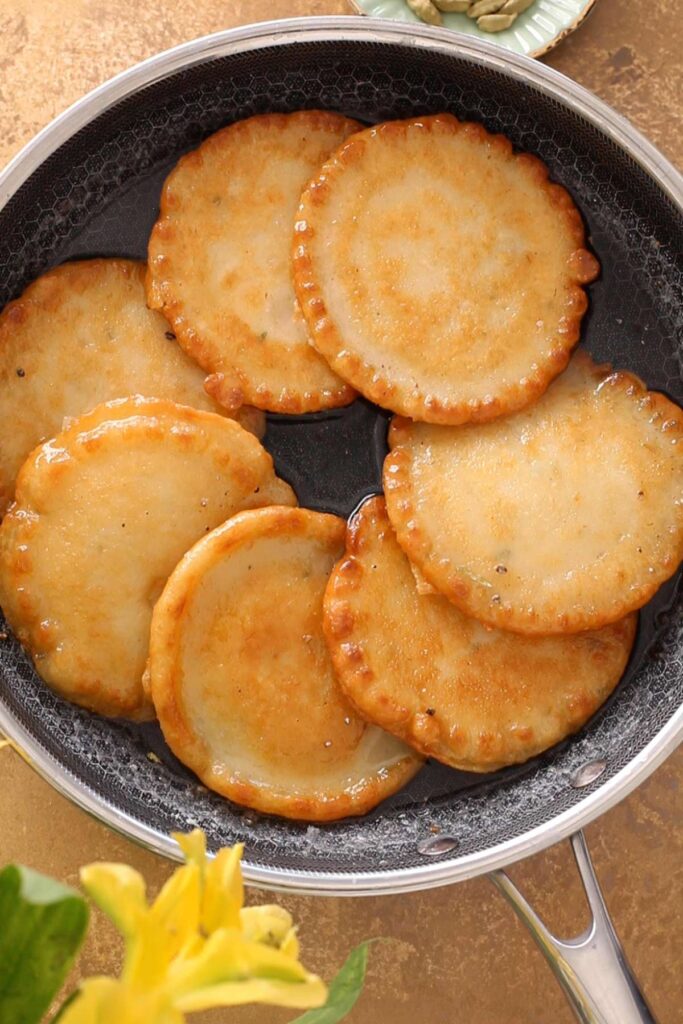 Malpua soaking in sugar syrup in a black pan.