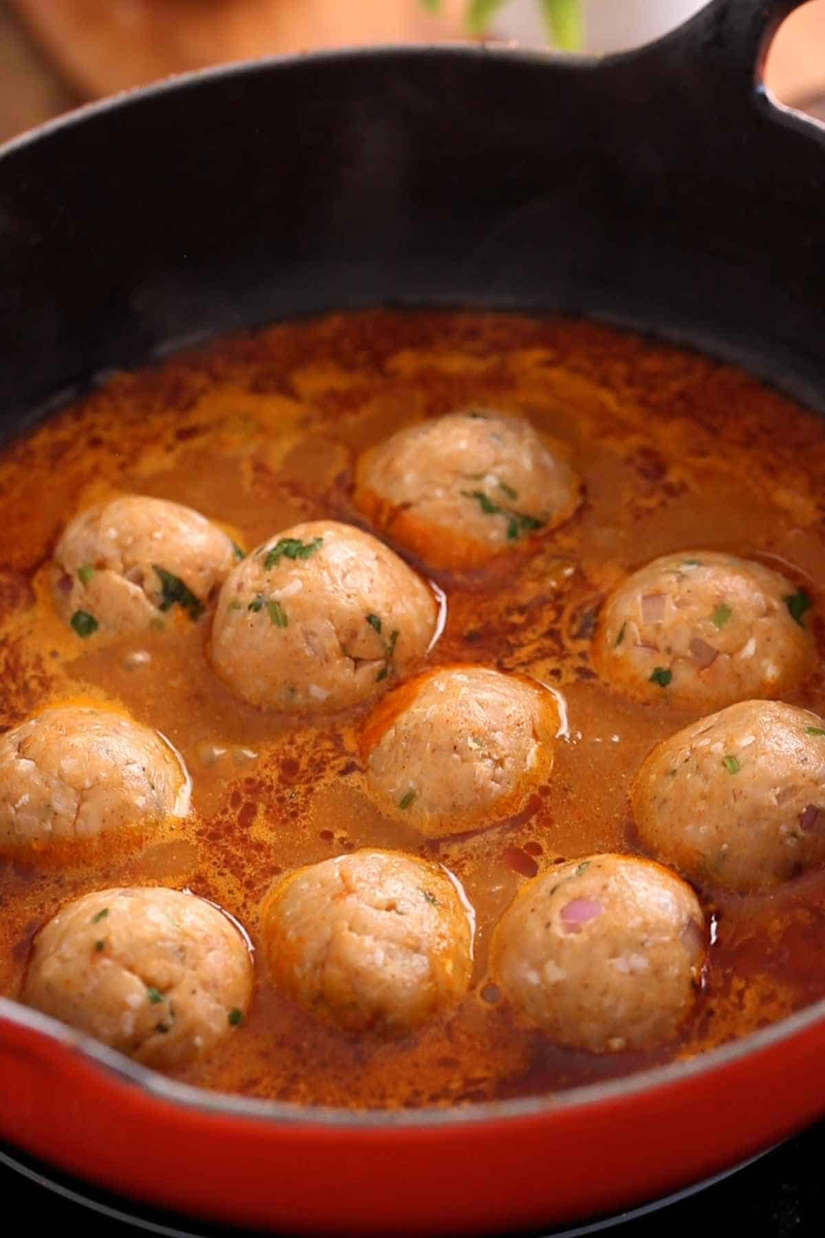 Raw chicken kofta are added to gravy in a single layer.