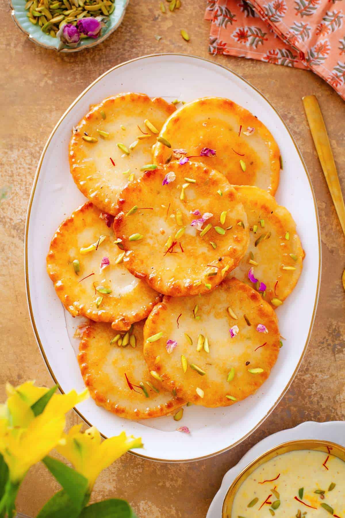 Malpua served in a white oval plate with a garnish of nuts and rose petals.