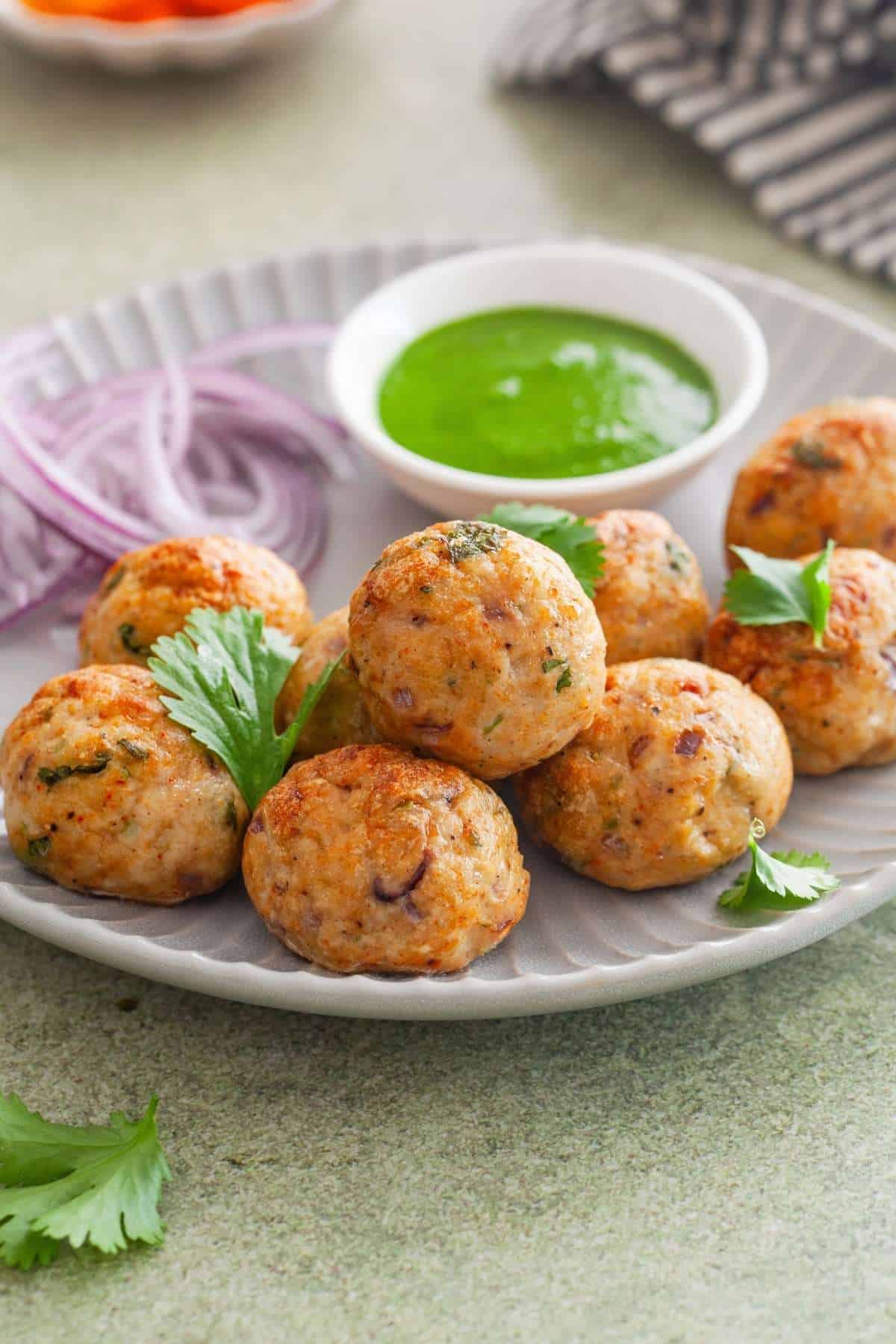 Chicken kofta meatballs served in a grey plate for snack with green chutney and sliced onions.