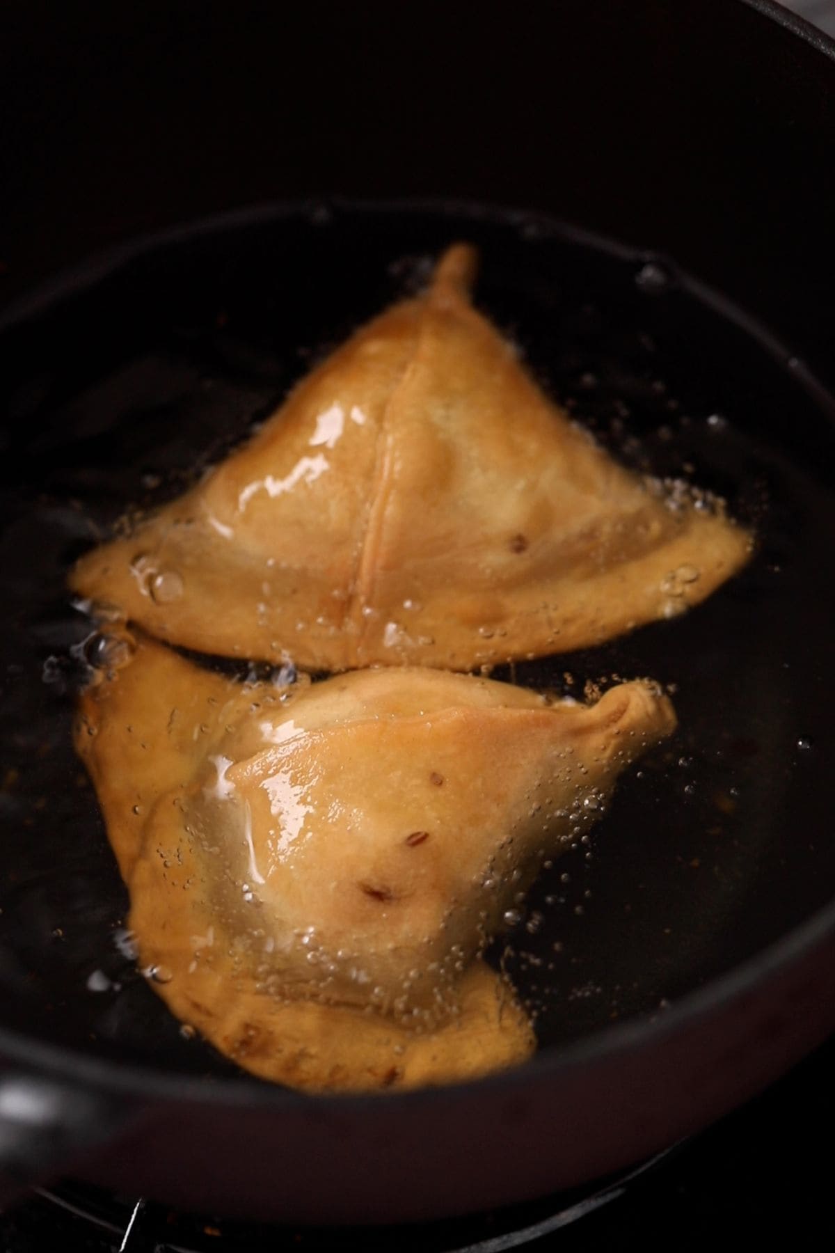 Samosa are deep frying in oil in a black wok. 