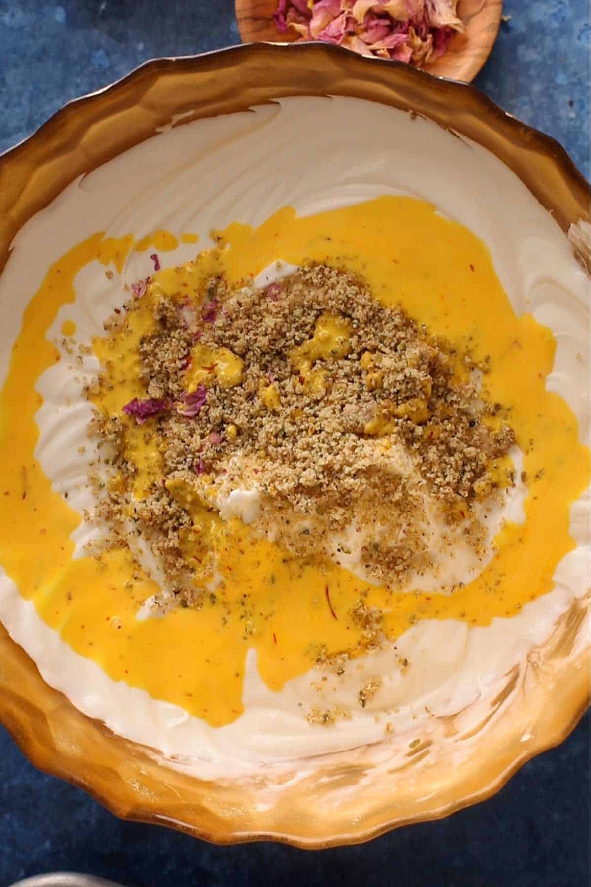 Thandai masala and saffron added to whipped mascarpone cream in a gold bowl.