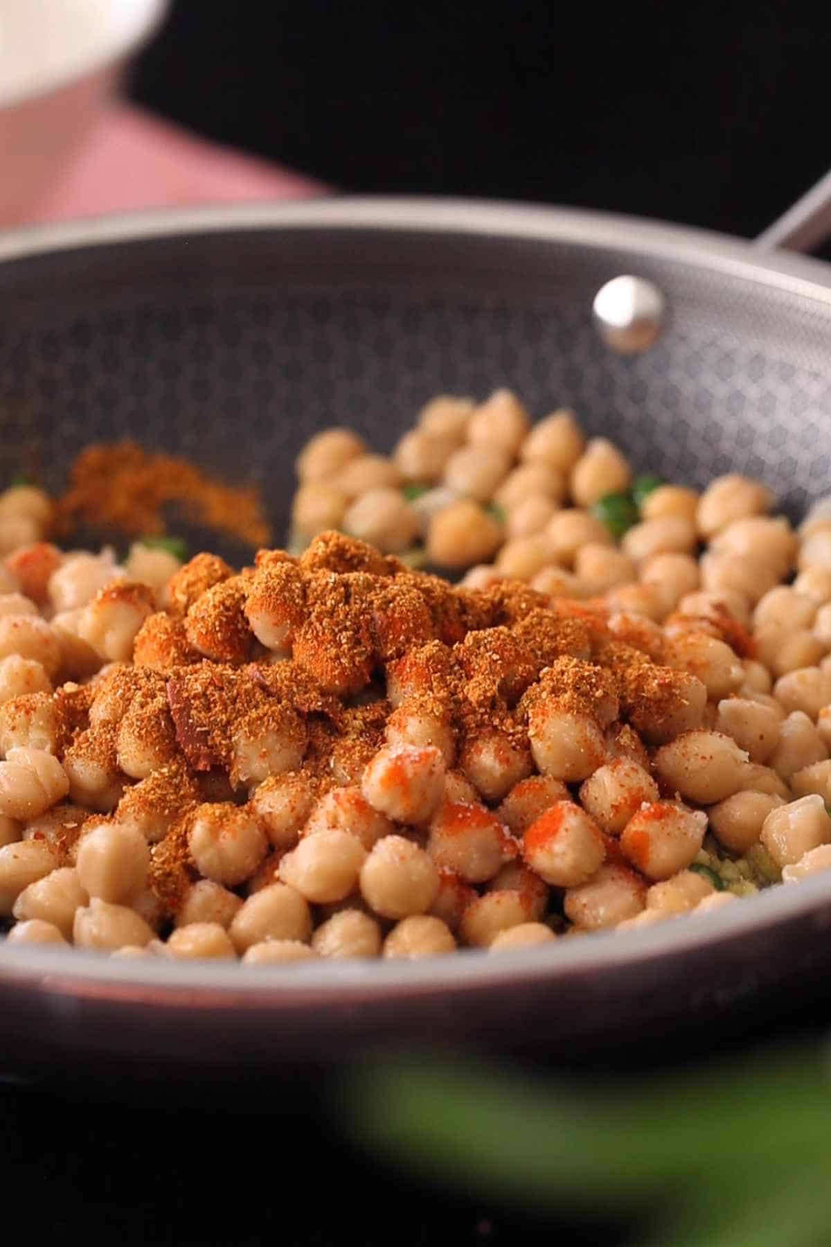 Boiled chickpeas added to cooking pan with ground spices.