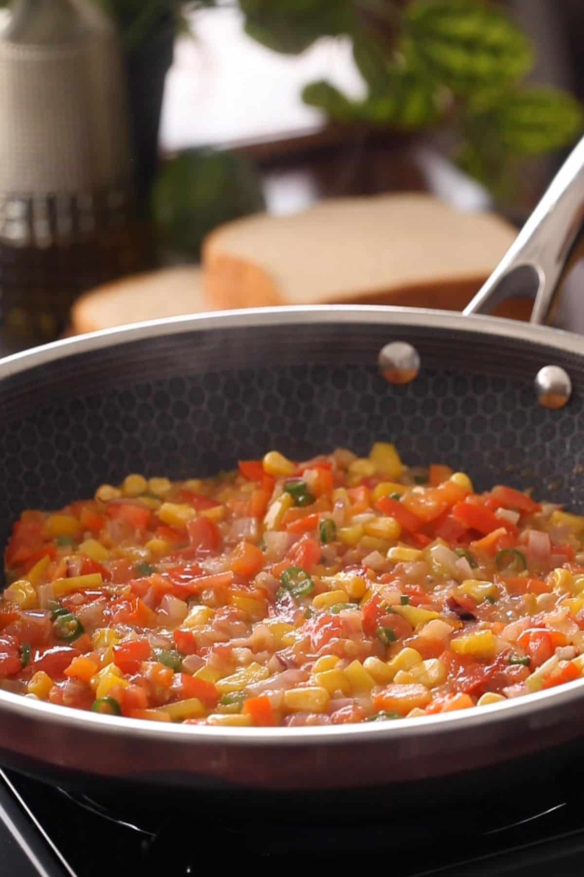 Cooked tomatoes and vegetables in black skillet.