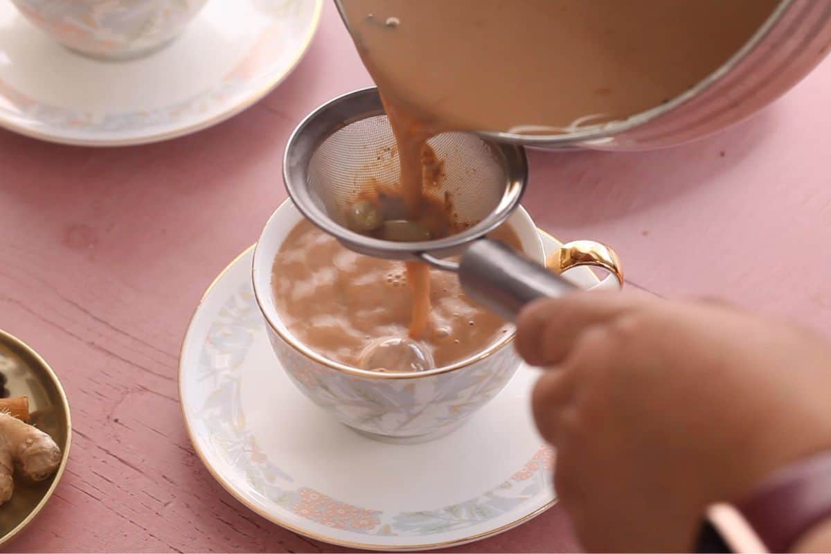 Straining indian chai in tea cups through a mesh strainer.
