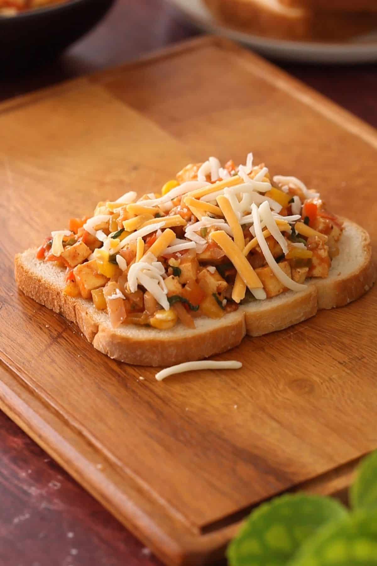 Paneer filling and shredded cheese on a bread slice.