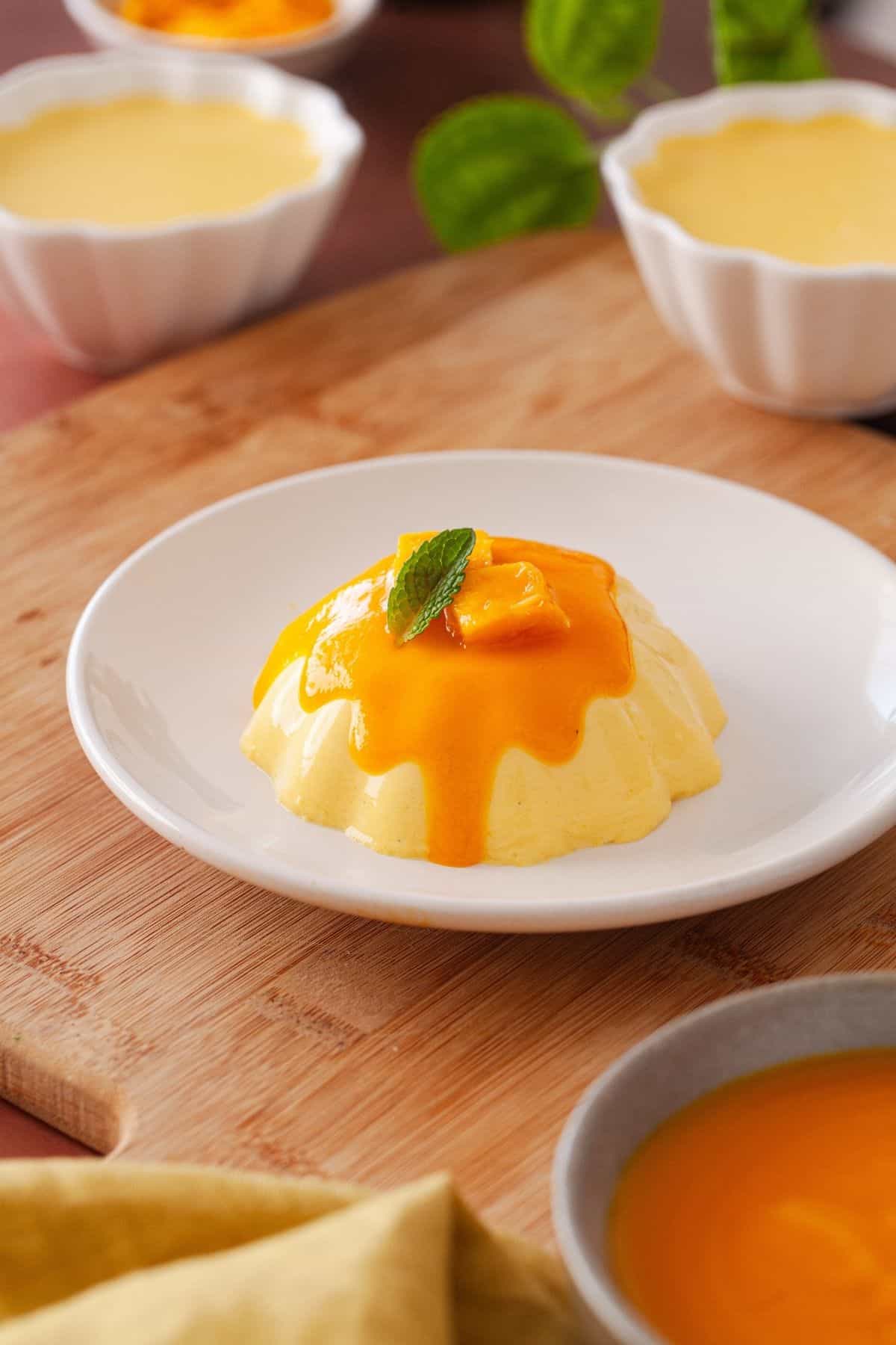 Mango Panna cotta served on a white plate with mango sauce and mango pieces.