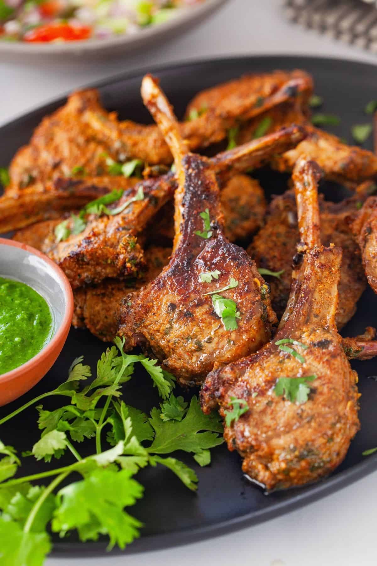 Front view of indian spiced lamb chops in a black platter.