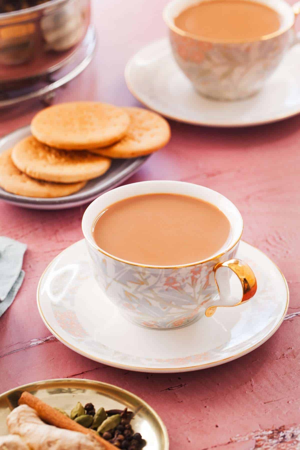 Masala Chai served with tea biscuits on a pink background.