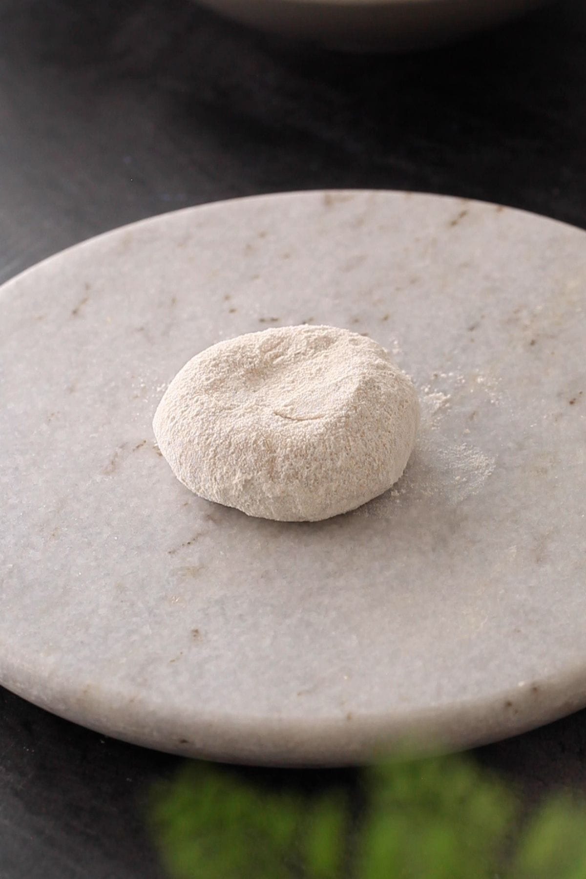 Ball of dough covered with dry flour on a round marble board.