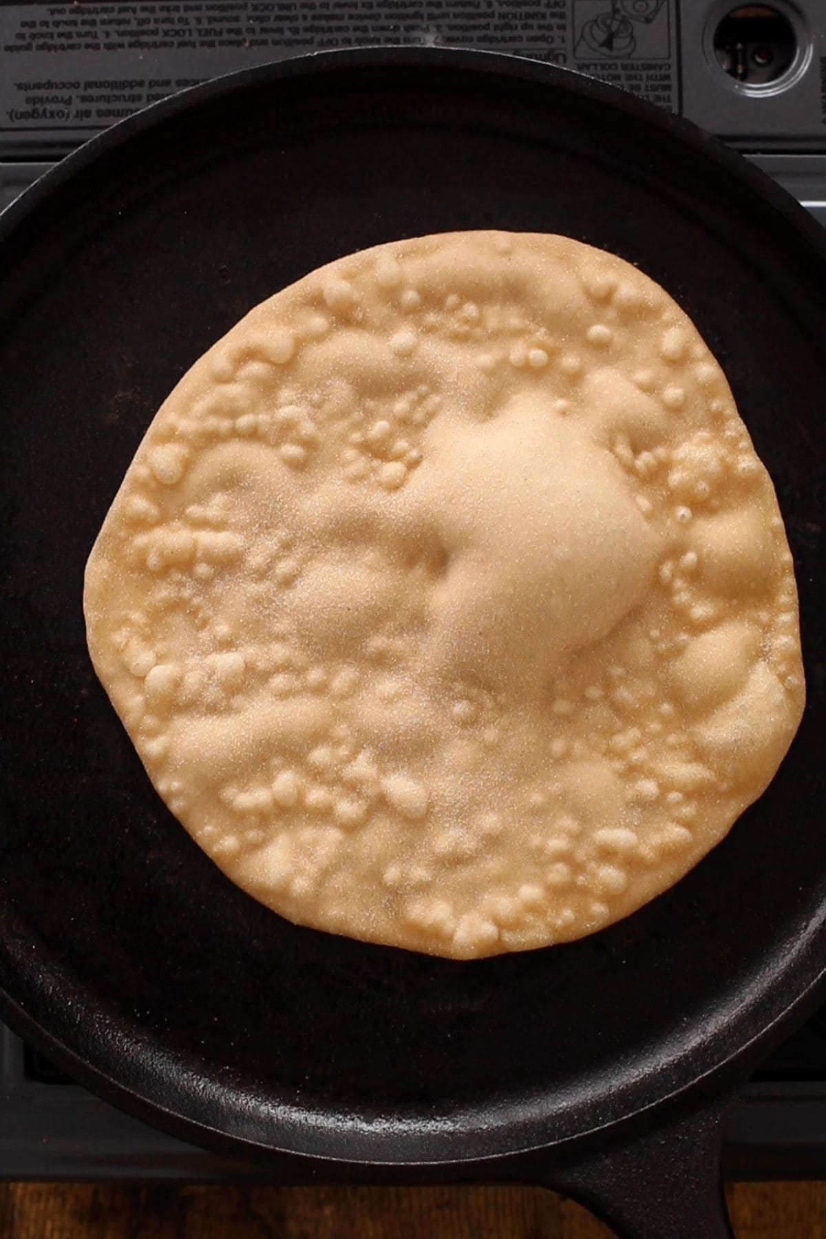 Tandoori roti with puffy spots on a cast iron griddle.